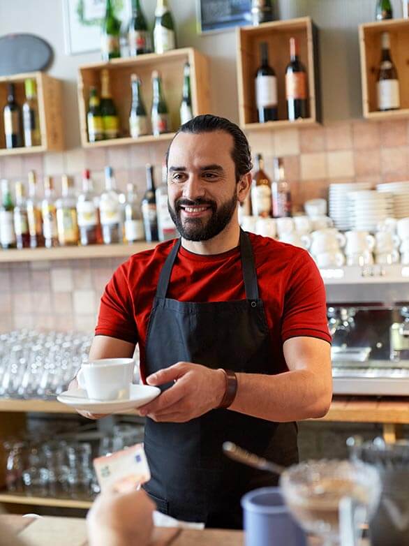 Cafe employee smiles while handing cup of coffee to patron