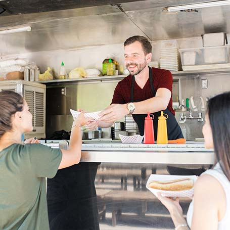 Food truck owner hands hotdog to patron