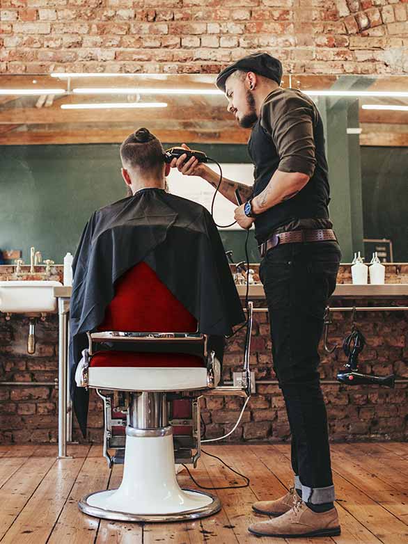 Barber trims hair of patron in trendy barbershop