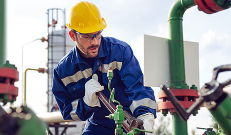 worker tightens valve near oil drilling
